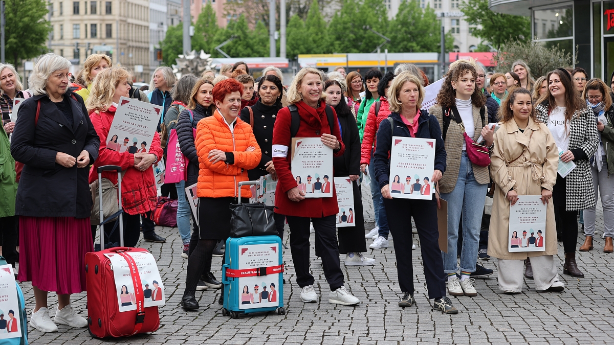 Frauen stehen mit Koffern und Plakaten auf einem Platz und demonstrieren