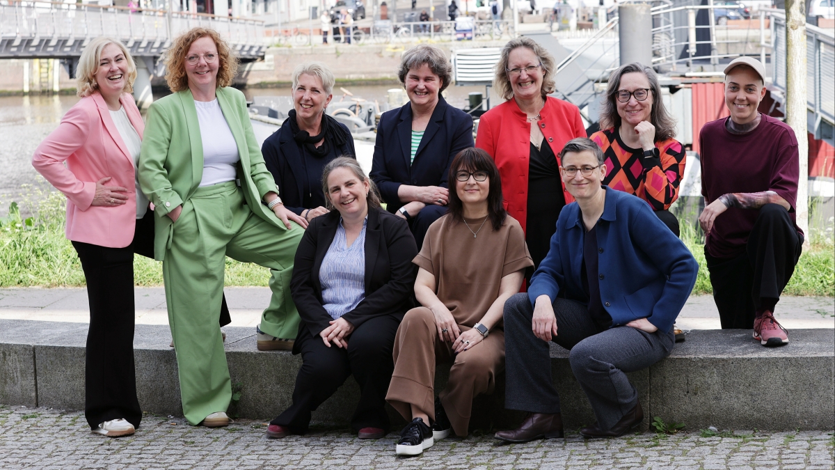Frauen sitzen und stehen gemeinsam vor einer Brücke