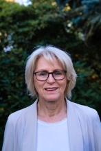 Frau mit kürzeren Haaren, Brille und Sakko vor Baum