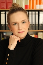 Frau mit zusammengesteckten Haaren vor einem Bücherregal und schwarzer Pulli