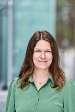 Frau mit braunen gewellten Haaren und grüner Bluse.