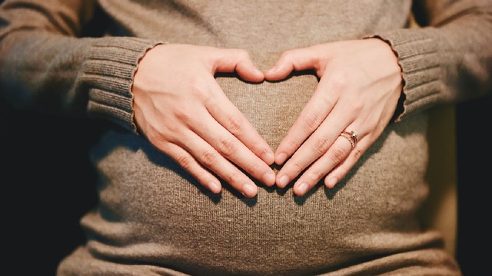 Bauch von schwangerer Frau, die mit den Händen ein Herz formt
