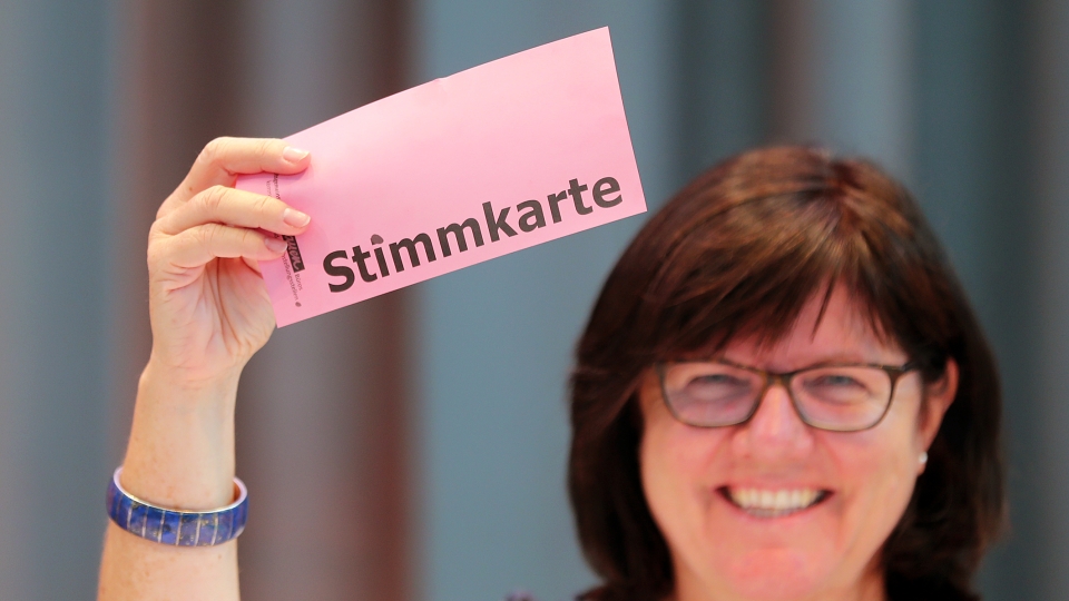 eine dunkelhaarige Frau hält Stimmzettel hoch