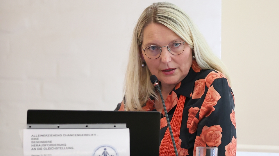 eine blonde Frau mit langen, glatten Haaren und Brille referiert