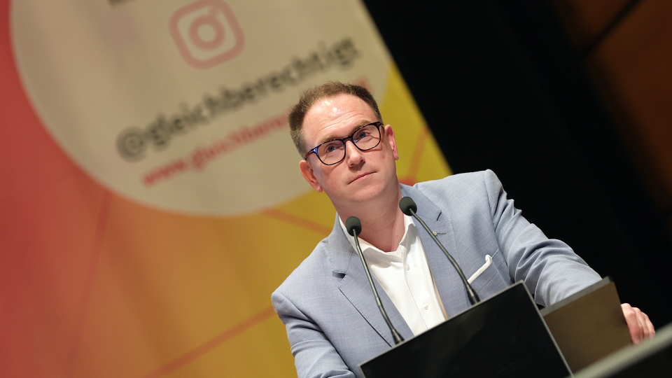 ein Mann mit hellblauem Anzug und Brill am Rednerpult