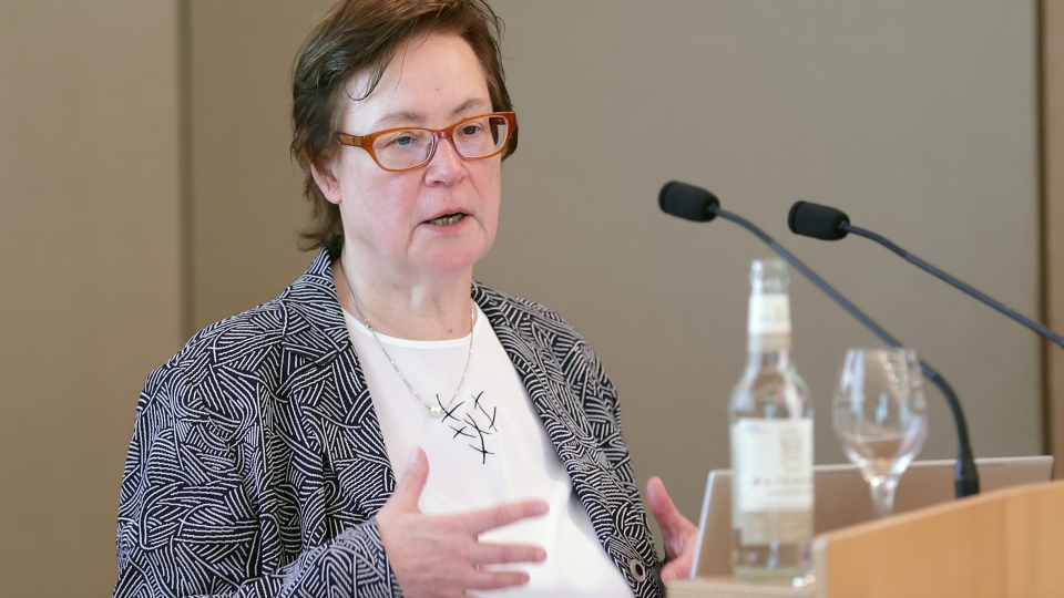 Frau mit Brille und kurzen braunen Haaren spricht am Mikro
