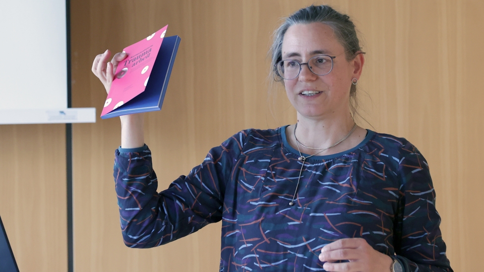 Frau mit Brille und hält Broschüre in die Luft