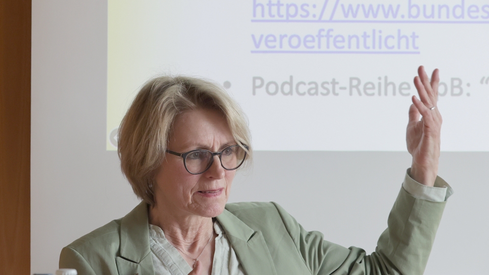 blonde kurzhaarige Frau mit Brille spricht mit erhobener Hand