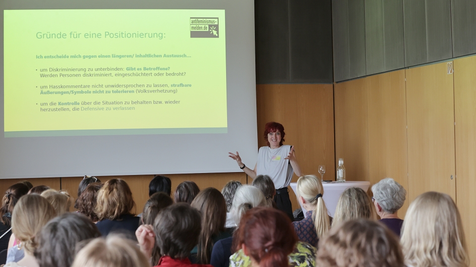 Präentation an der Wand , davor Referentin mit dunklen Haaren